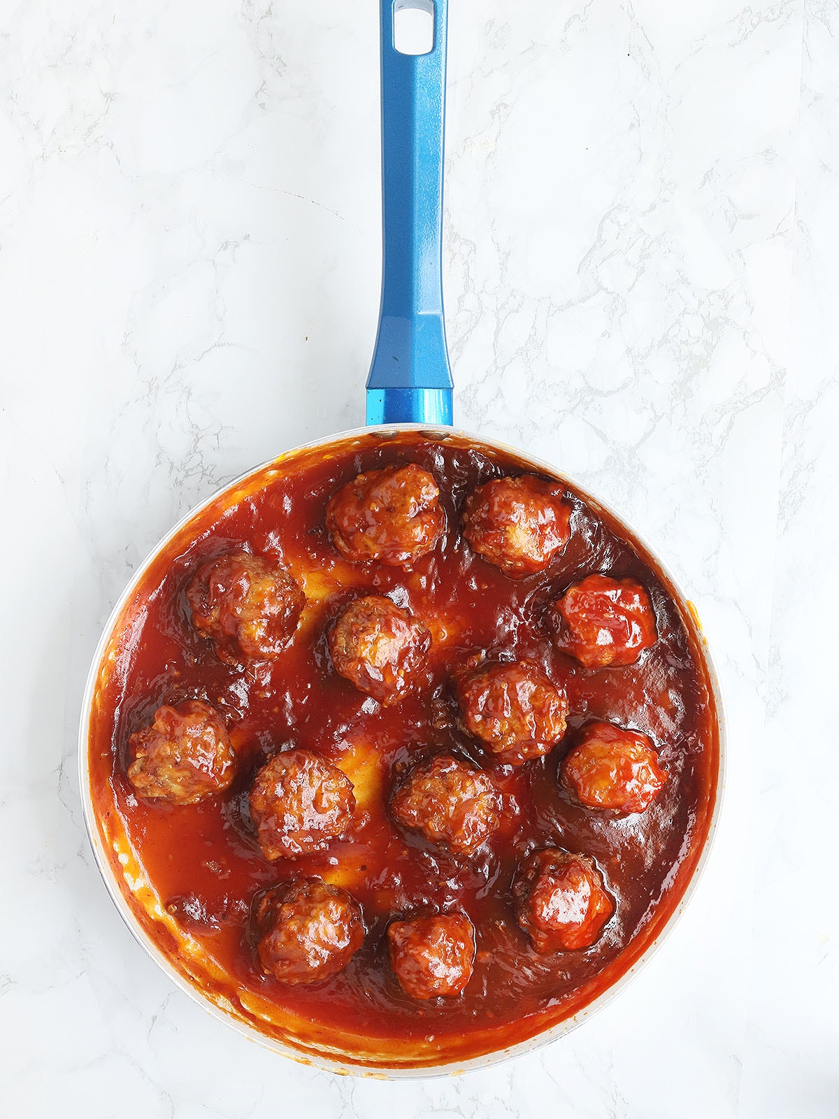 skillet of glazed meatballs on a white marble background