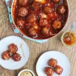 skillet of glazed meatballs with two plates containing three meatballs each to the side