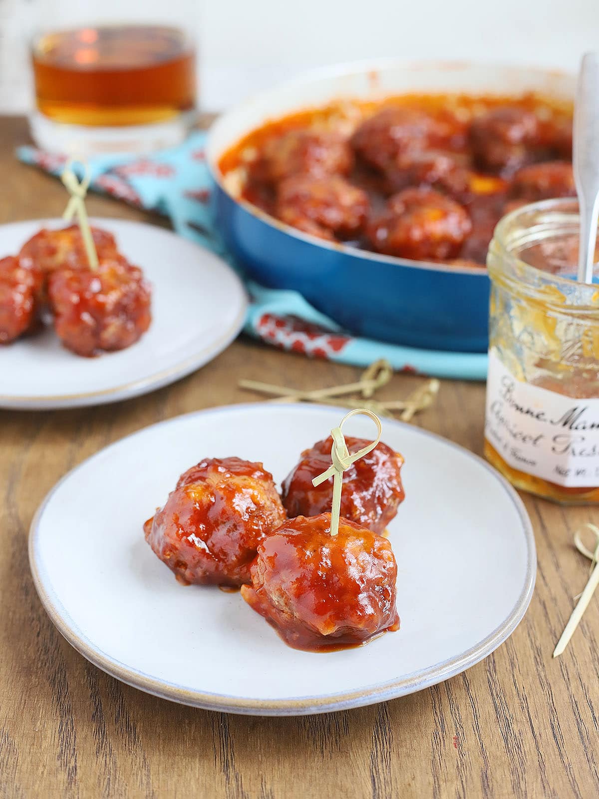 three glazed meatballs on a plate with a pan of meatballs in the background