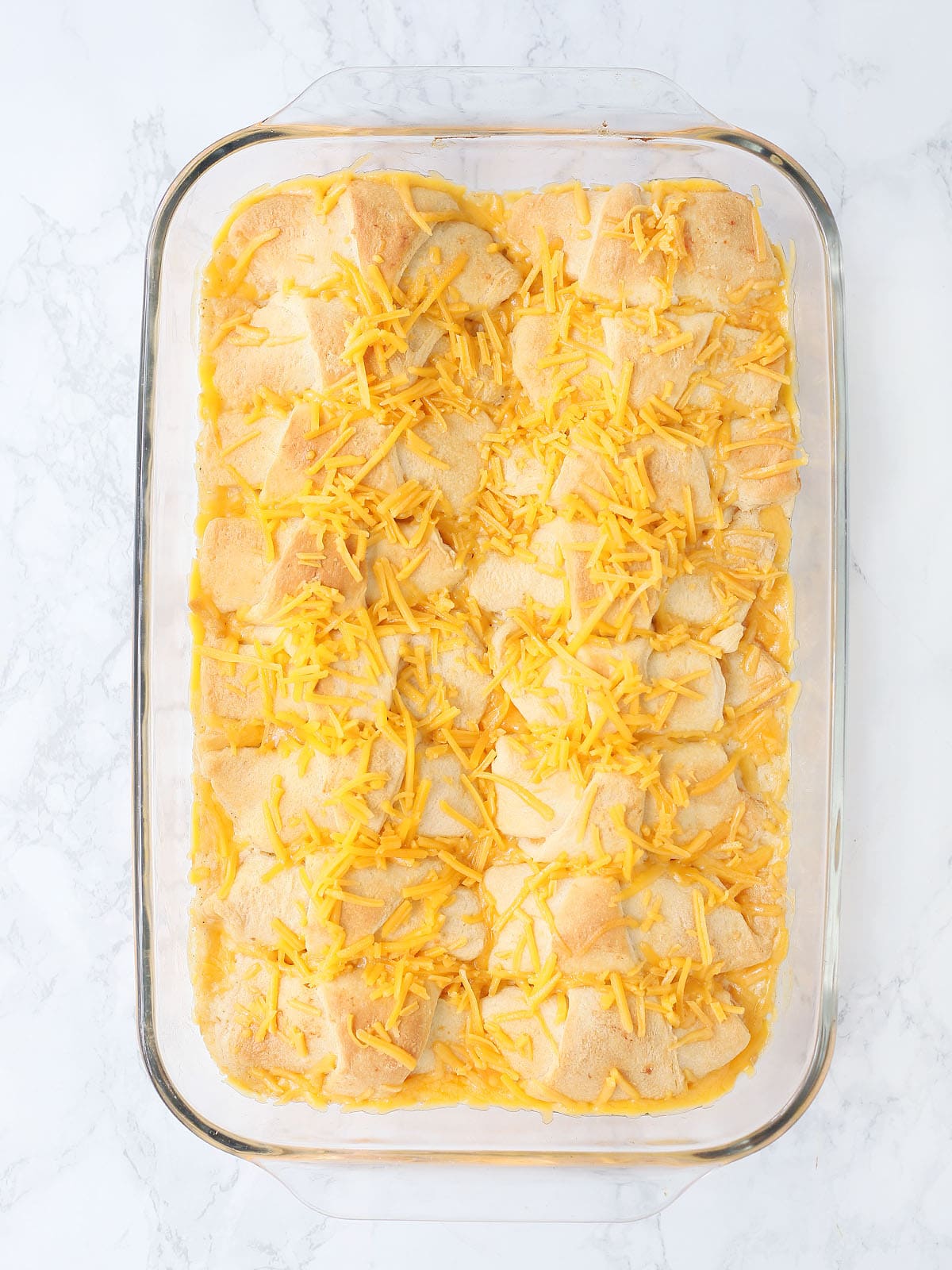 unbaked crescent chicken topped with cheese in a glass casserole dish
