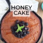 honey cake in a cast iron skillet topped with fresh black berries and drizzled with honey