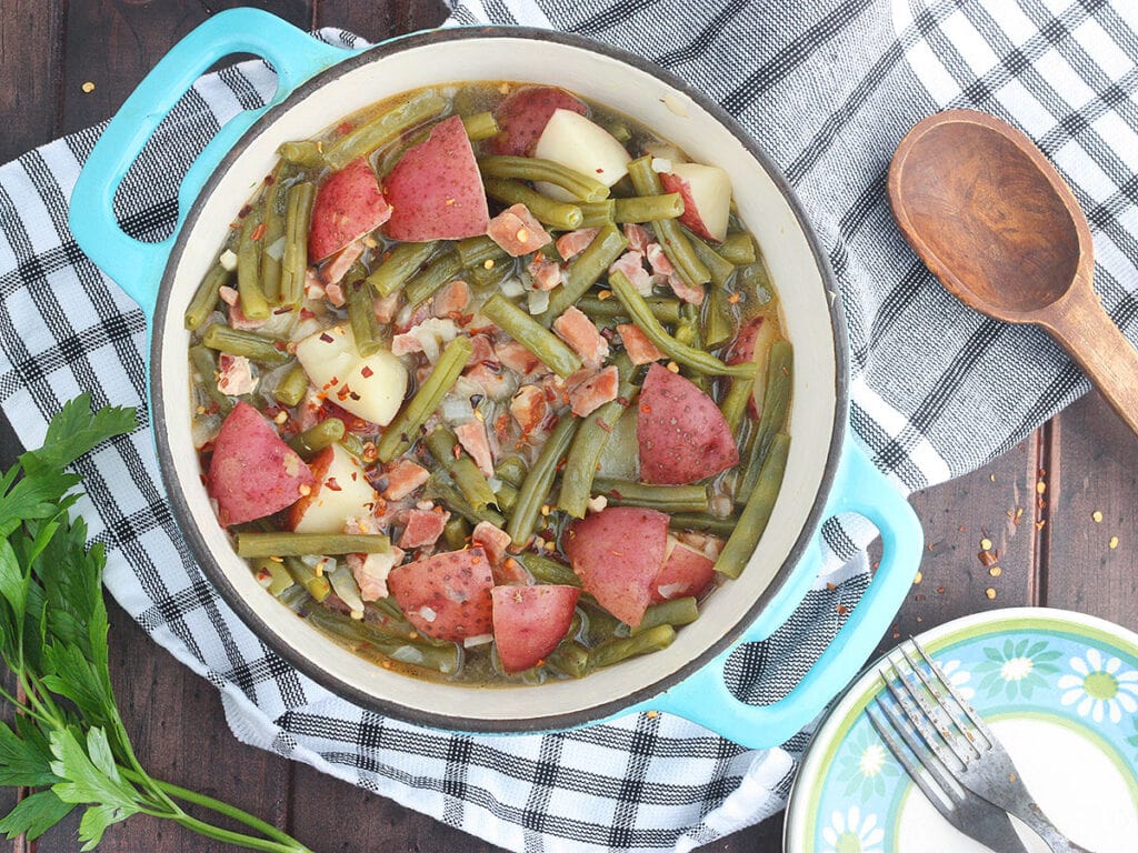 light blue pot full of green beans and potatoes with a plate and serving spoon to the side
