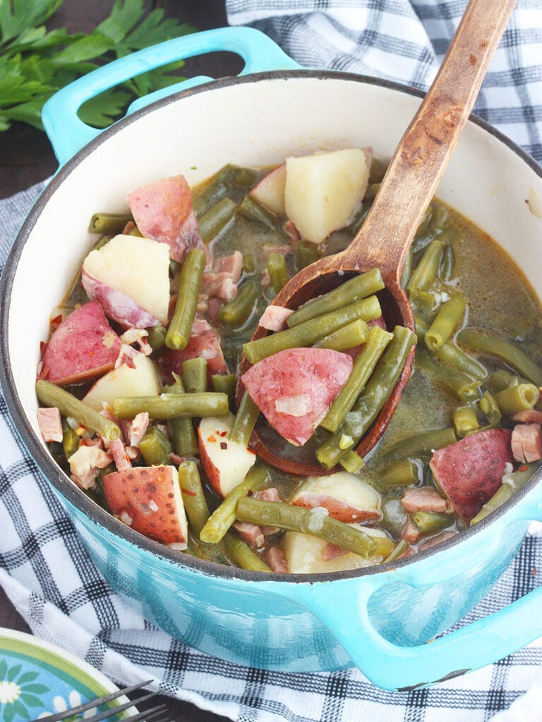 blue pot full of green beans and potatoes being served with a wooden spoon