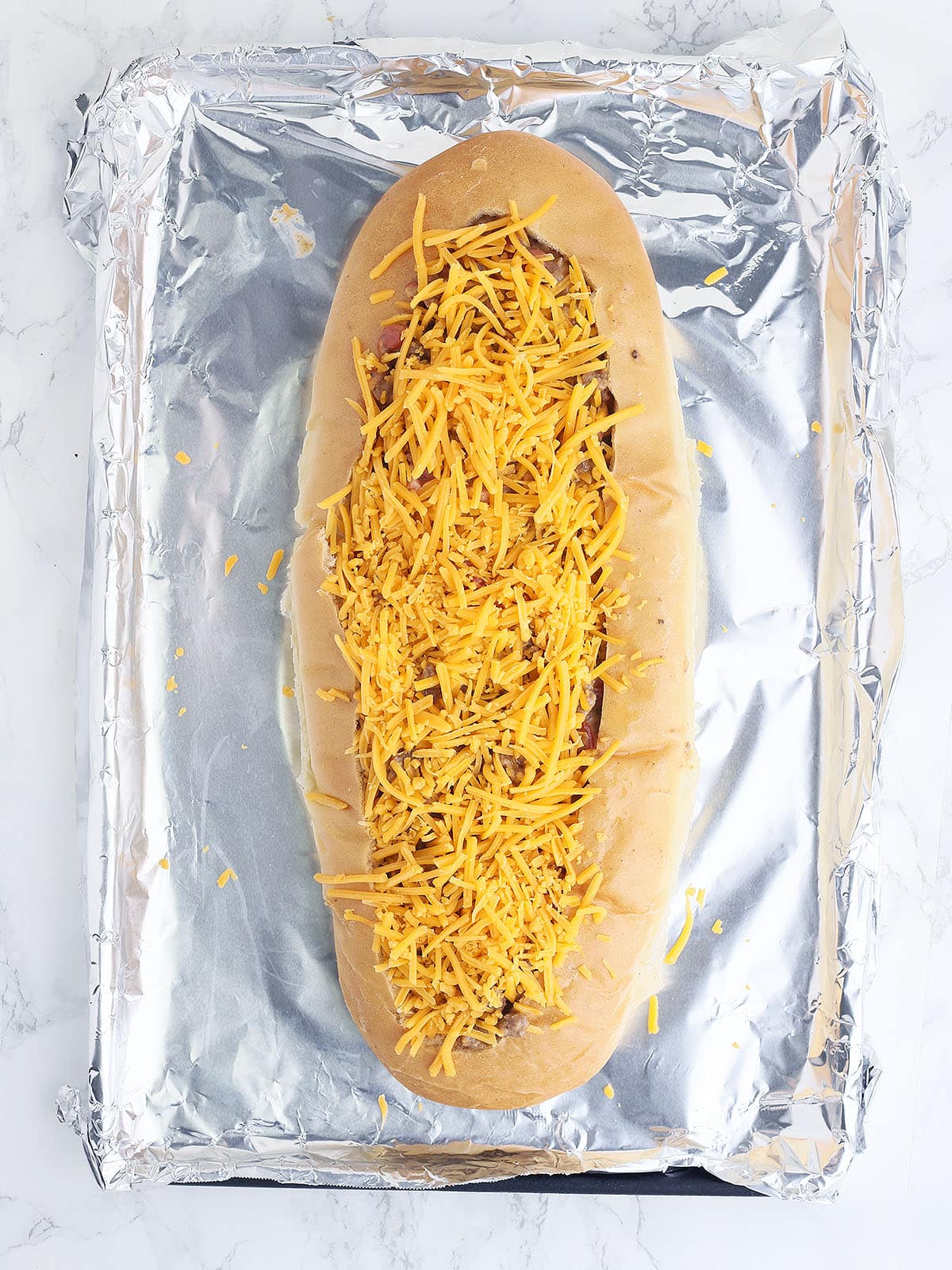 unbaked bacon cheeseburger stuffed French bread topped with shredded cheddar cheese