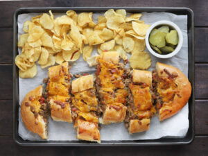sliced bacon cheeseburger stuffed French bread on a parchment paper lined baking sheet