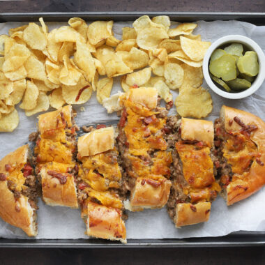 sliced bacon cheeseburger stuffed French bread on a parchment paper lined baking sheet