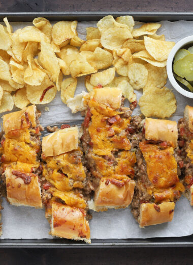 sliced bacon cheeseburger stuffed French bread on a parchment paper lined baking sheet