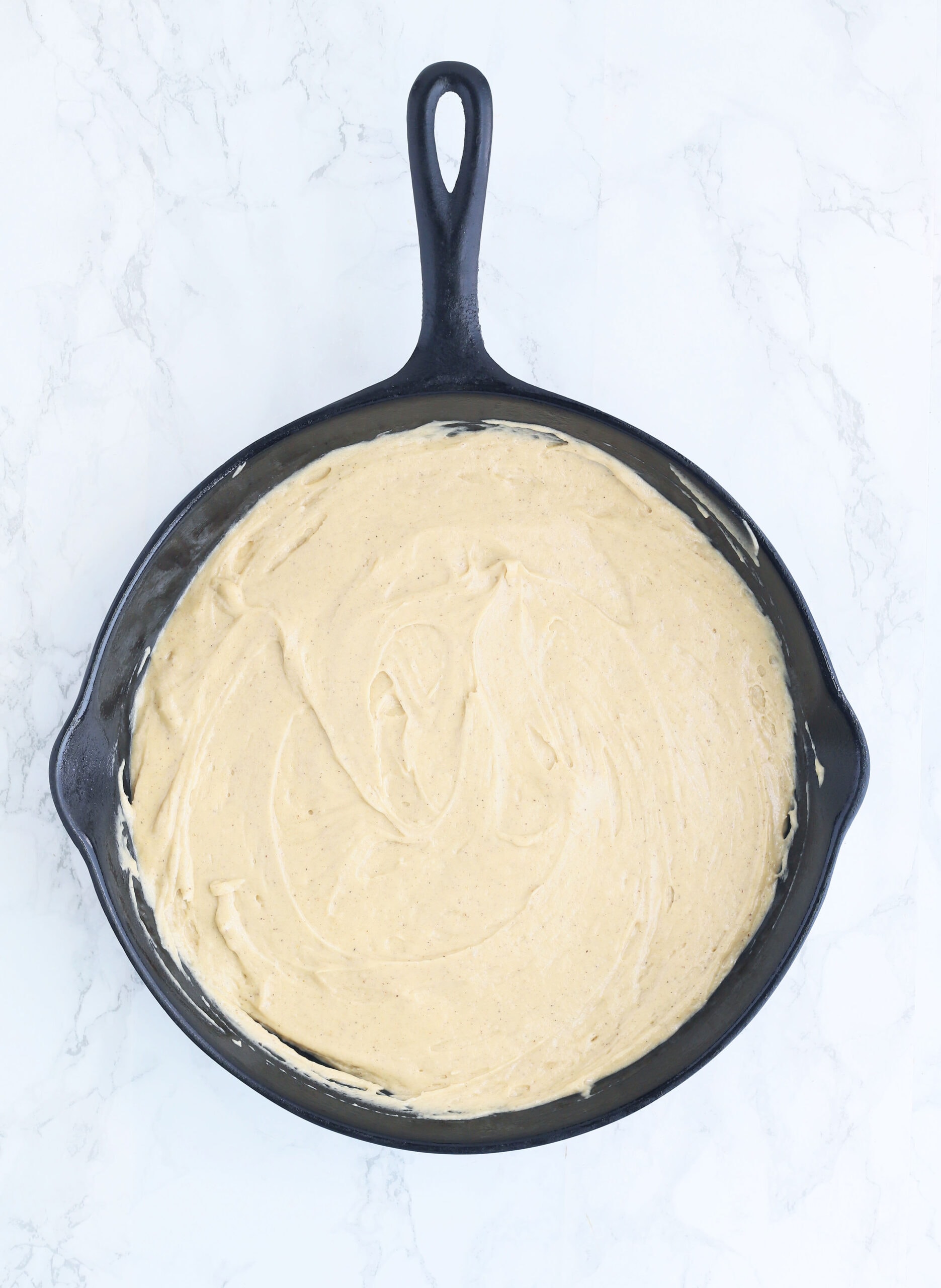 honey cake batter spread into the bottom of a cast iron skillet