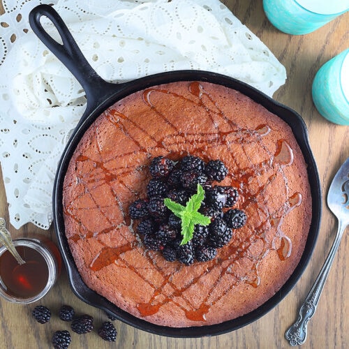 Honey cake in a cast iron skillet topped with fresh black berries and drizzled with honey