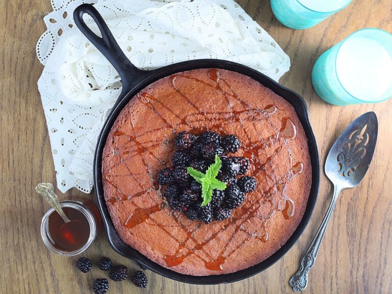 Honey cake in a cast iron skillet topped with fresh black berries and drizzled with honey