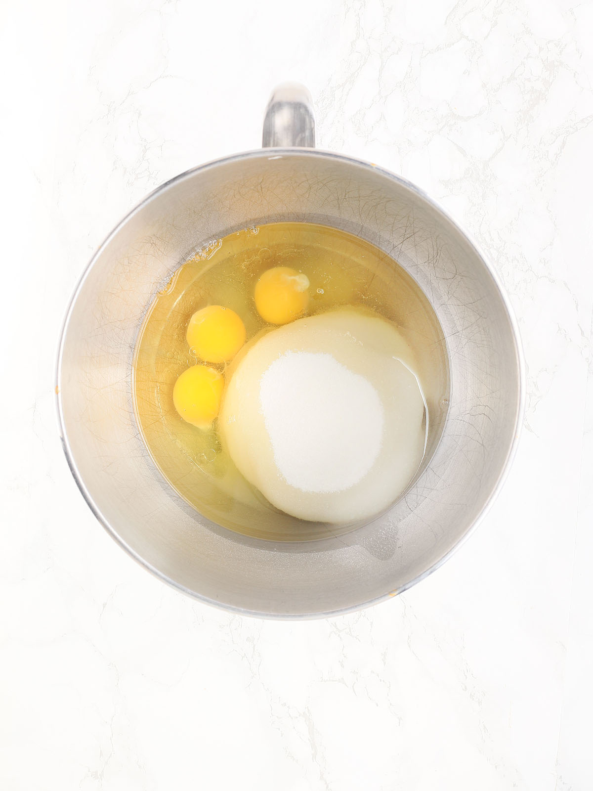 three eggs, sugar and oil unmixed in a metal mixing bowl