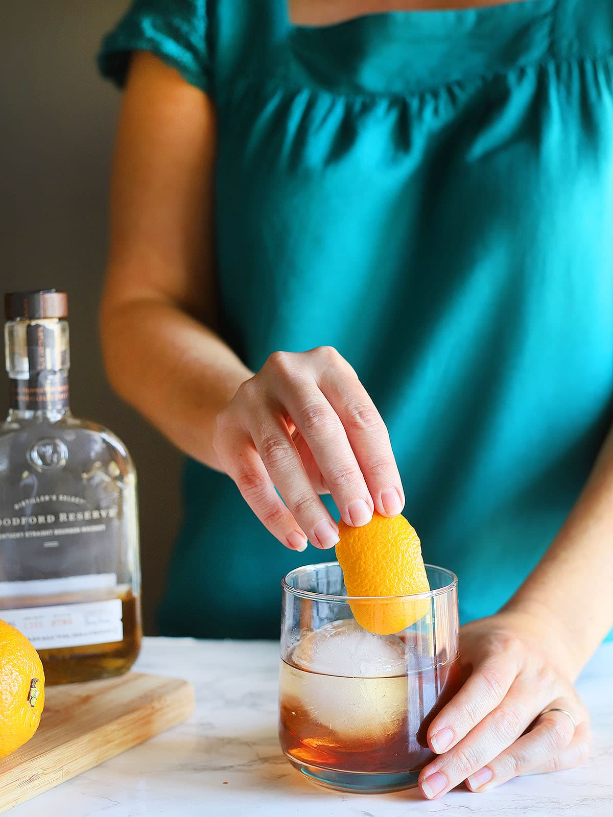 hand garnishing a bourbon old fashioned with an orange peel