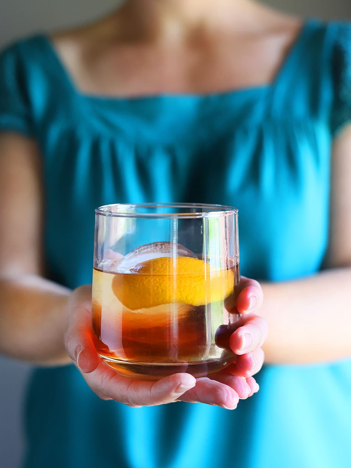 hand holding out a rocks glass with a bourbon old fashioned