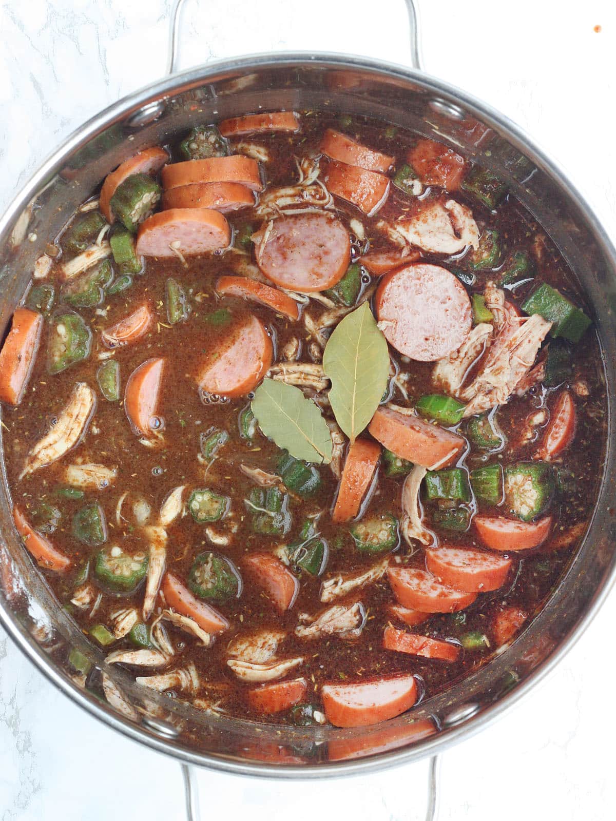 chicken and sausage gumbo in a steel pot with two bay leaves laying on top
