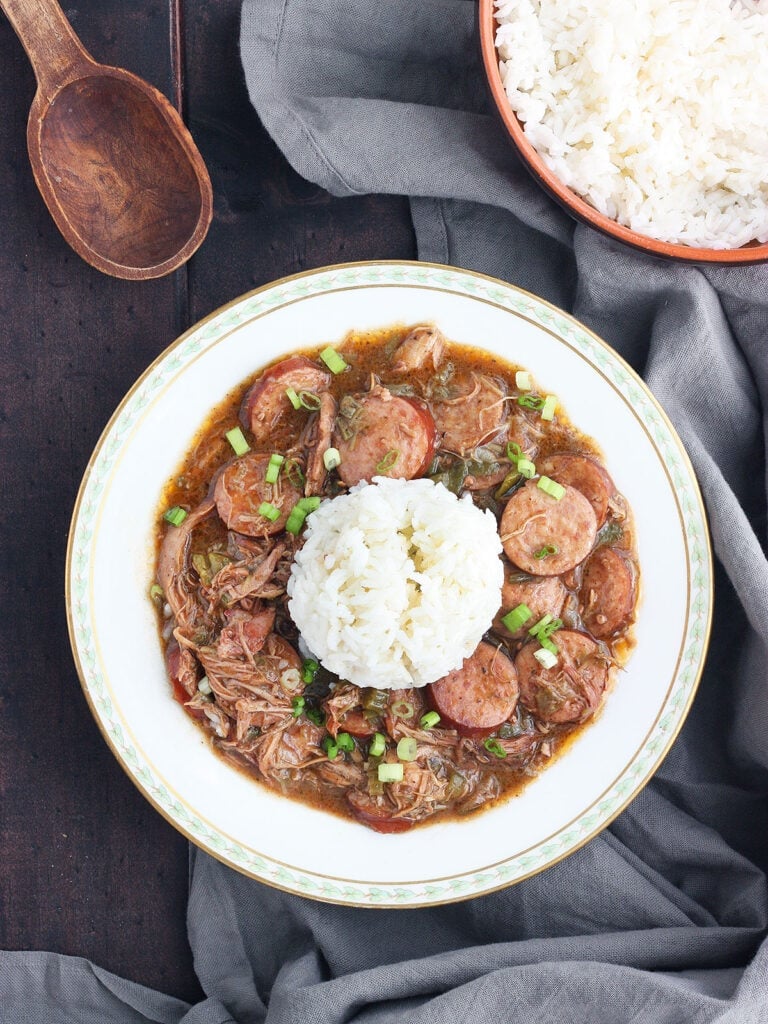 chicken and sausage gumbo with rice in a white bowl trimmed with green leaves