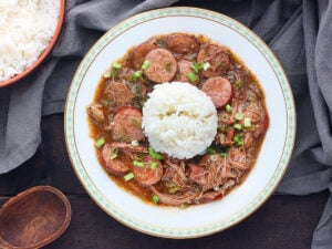 chicken and sausage gumbo with rice in a white bowl trimmed with green leaves