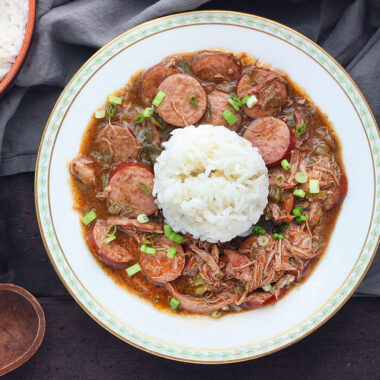 chicken and sausage gumbo with rice in a white bowl trimmed with green leaves