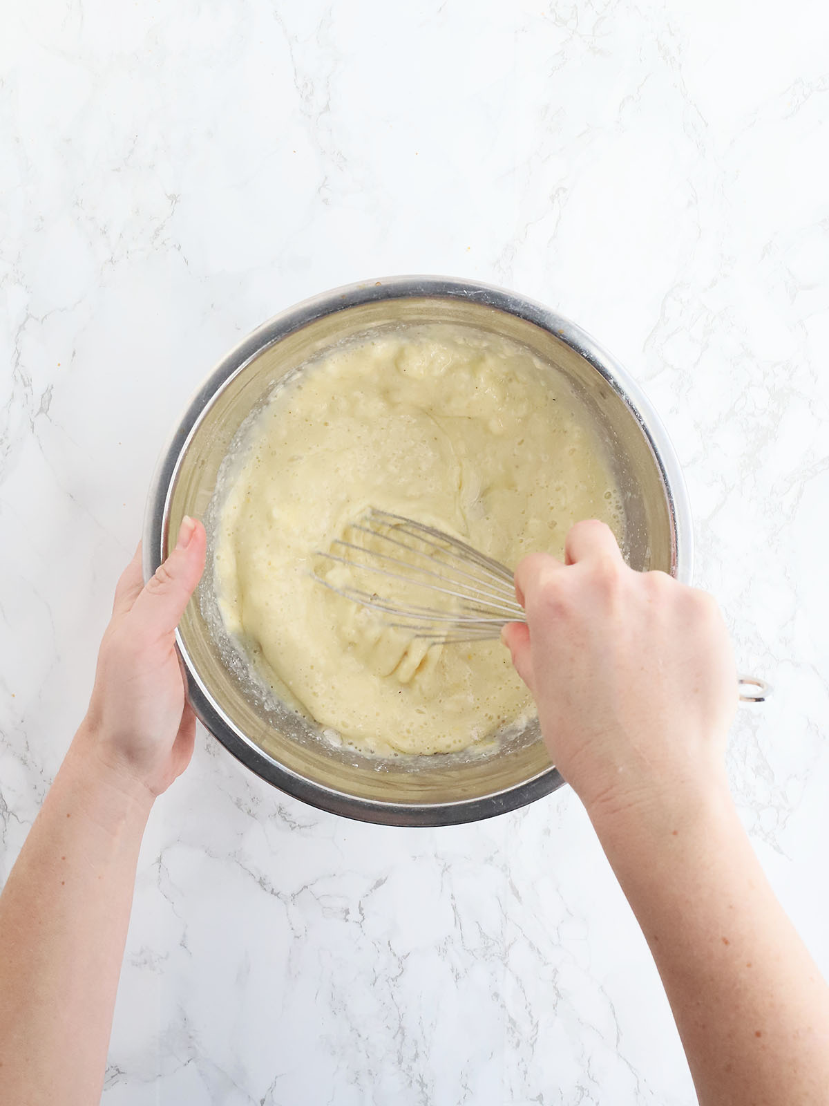 Hand whisking together cornbread batter in a metal mixing bowl.
