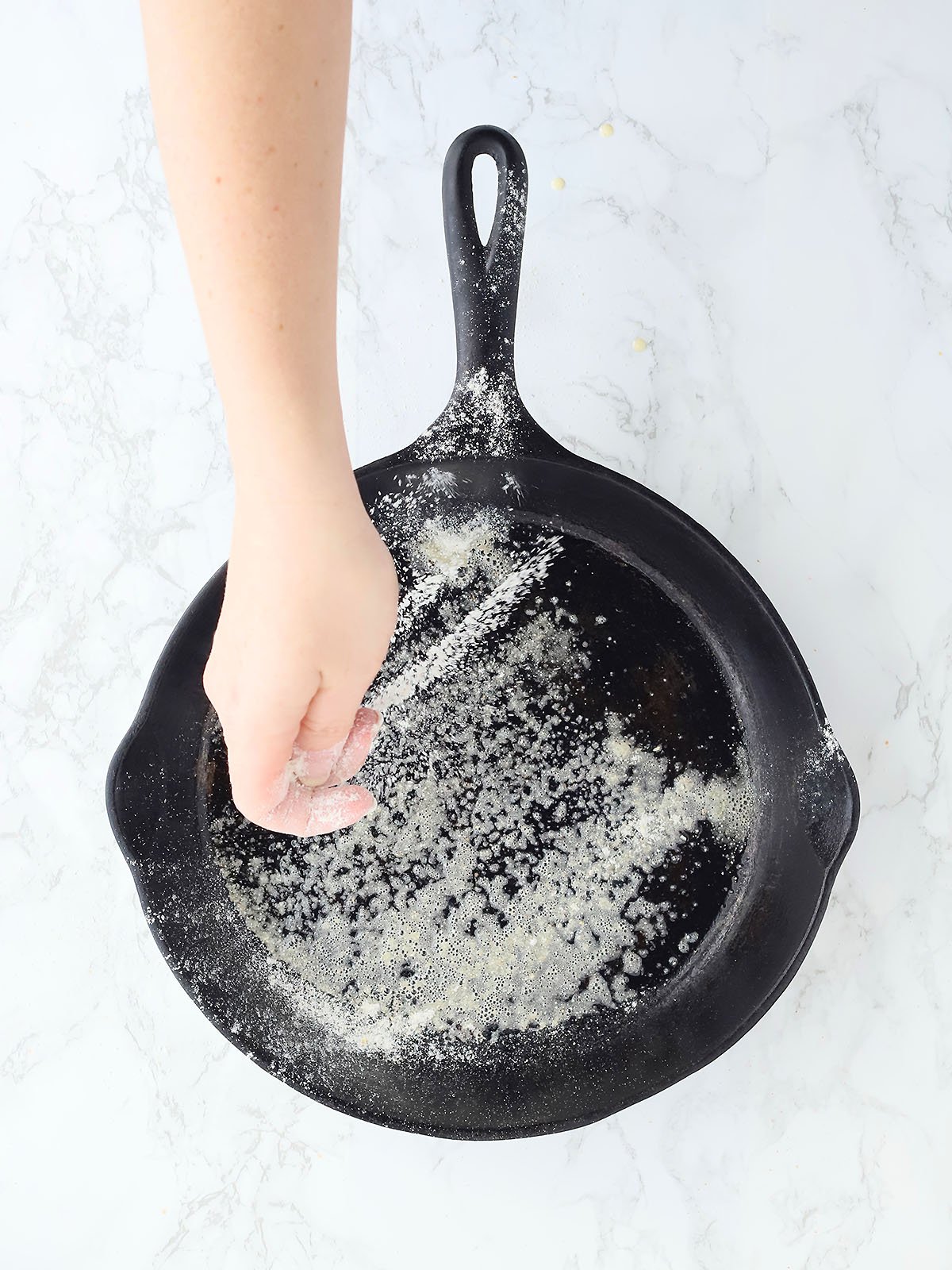 Hand sprinkling flour onto a greased cast iron skillet.