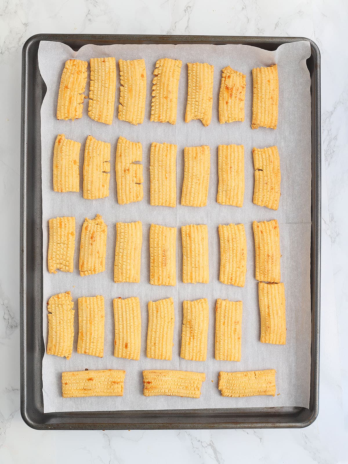 baked cheese straws cooling on a baking sheet.