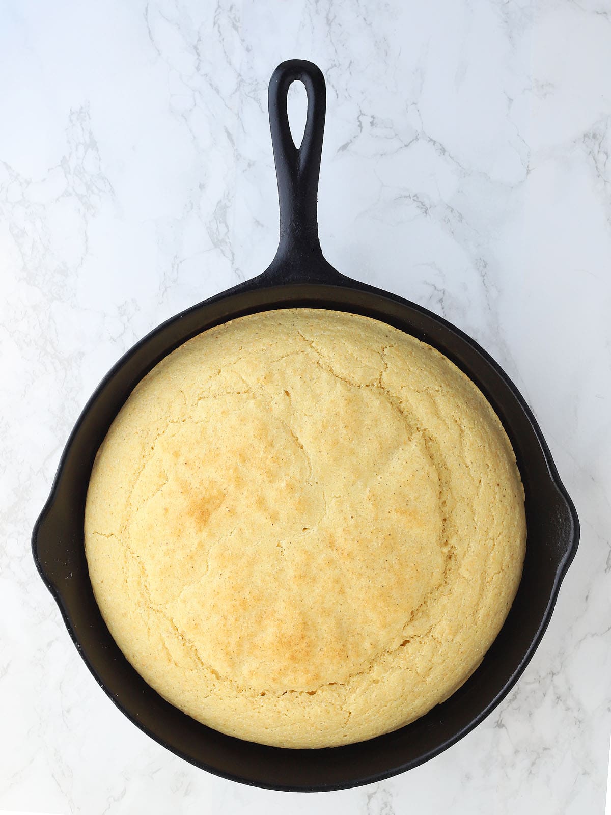 Baked cornbread in a cast iron skillet on a white background.