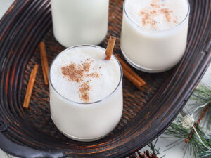 two glasses of bourbon milk punch garnished with nutmeg and cinnamon sticks on a wooden tray