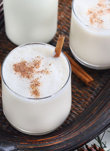 two glasses of bourbon milk punch garnished with nutmeg and cinnamon sticks on a wooden tray