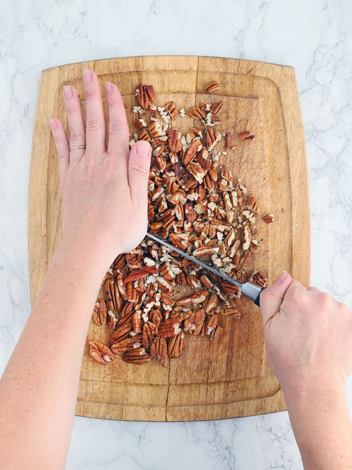 hands finely chopping pecans on a wooden cutting board