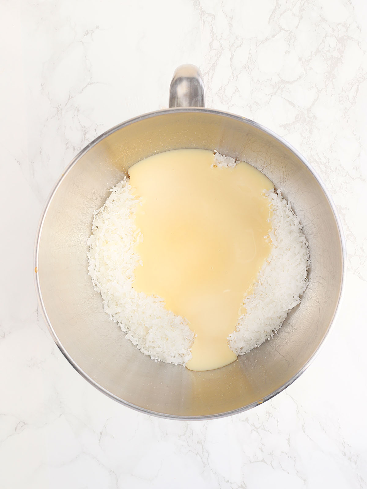 condensed milk and coconut in a metal mixing bowl before it has been whisked together