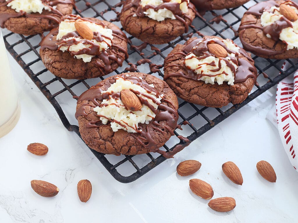 Almond Joy cookies on a wire baking rack with whole toasted almonds and a glass of milk to the side