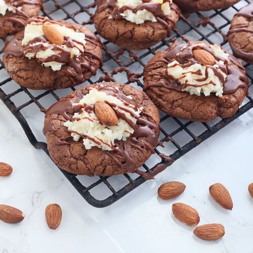 Almond Joy cookies on a wire baking rack with whole toasted almonds and a glass of milk to the side