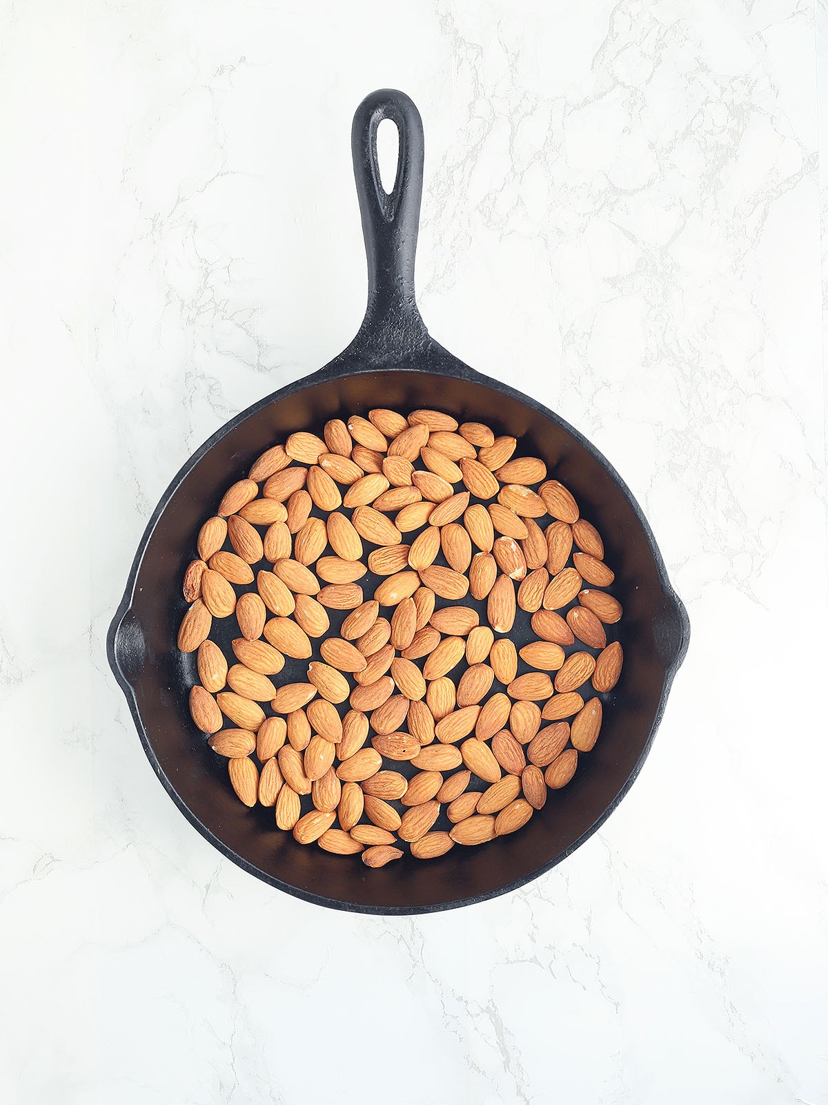 untoasted almonds in a cast iron skillet on a white background