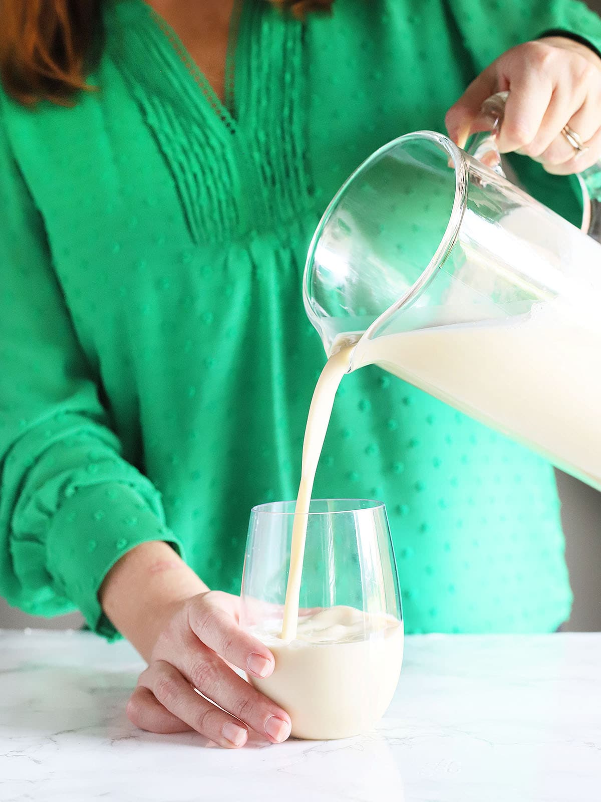 person pouring eggnog from a glass pitcher into a glass