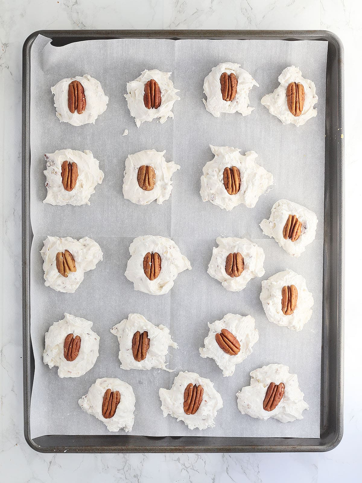 homemade divinity candy topped with pecans on a parchment paper lined baking sheet