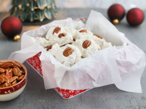 homemade divinity candy arranged in a paper lined candy tin with Christmas decorations in the background