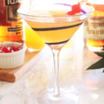 Tuaca pineapple martini garnished with two cherries with martini ingredients in the background