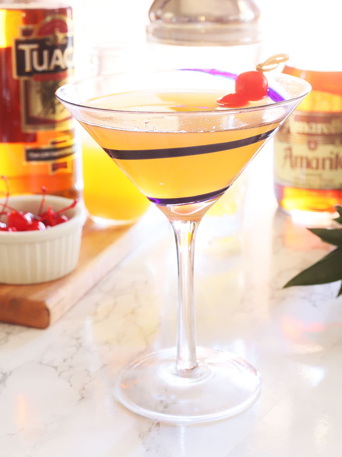 Tuaca pineapple martini garnished with two cherries with martini ingredients in the background