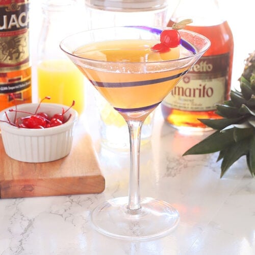 Tuaca pineapple martini garnished with two cherries with martini ingredients in the background