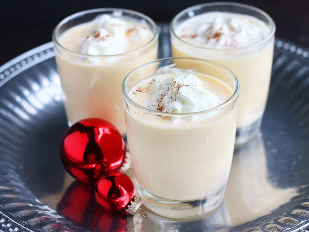 three glasses of bourbon eggnog on a silver tray decorated with red Christmas ornaments