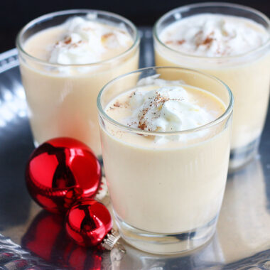 three glasses of bourbon eggnog on a silver tray decorated with red Christmas ornaments