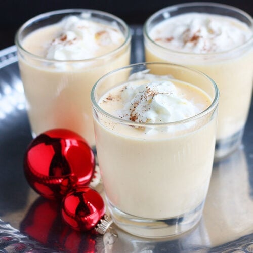 three glasses of bourbon eggnog on a silver tray decorated with red Christmas ornaments