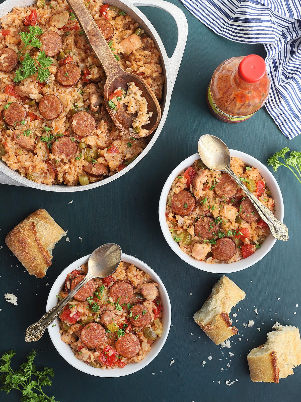 A serving dish and two bowls of chicken jambalaya with crust bread broken on the side