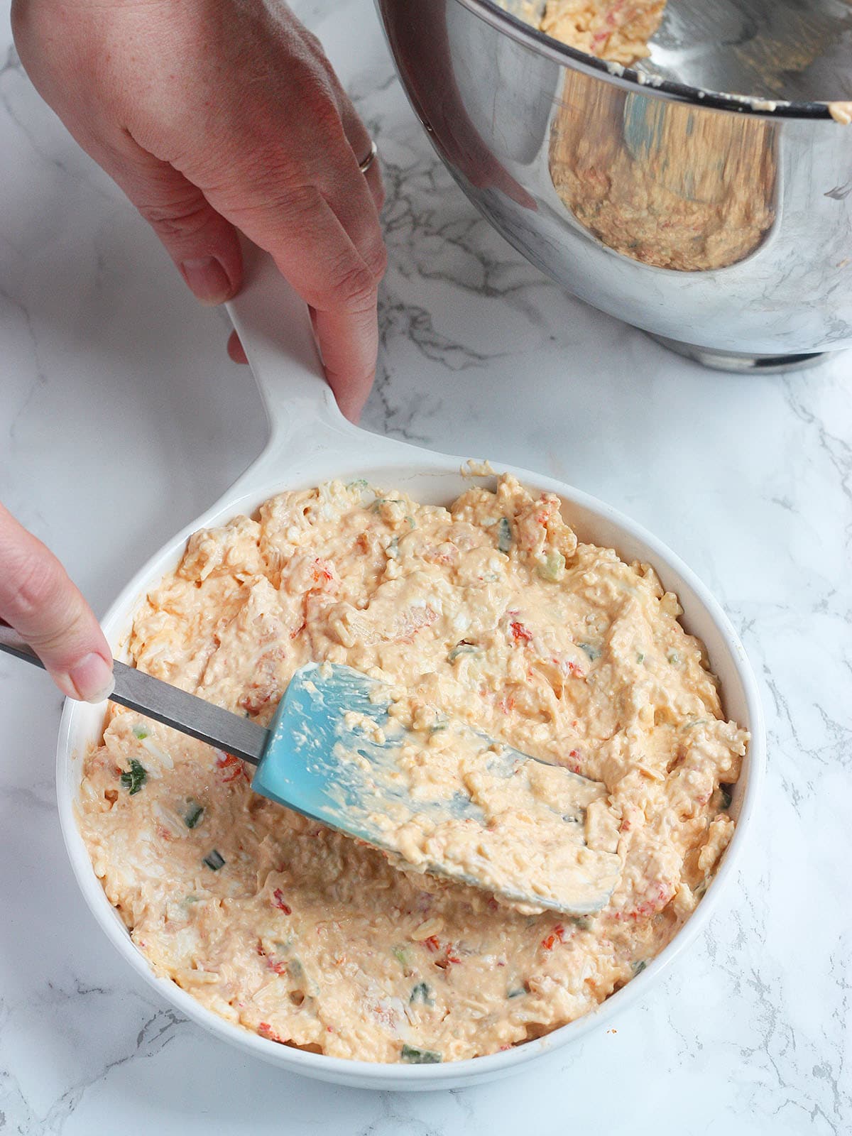 Using a spatula to spread the crawfish dip into an oven safe baking dish.