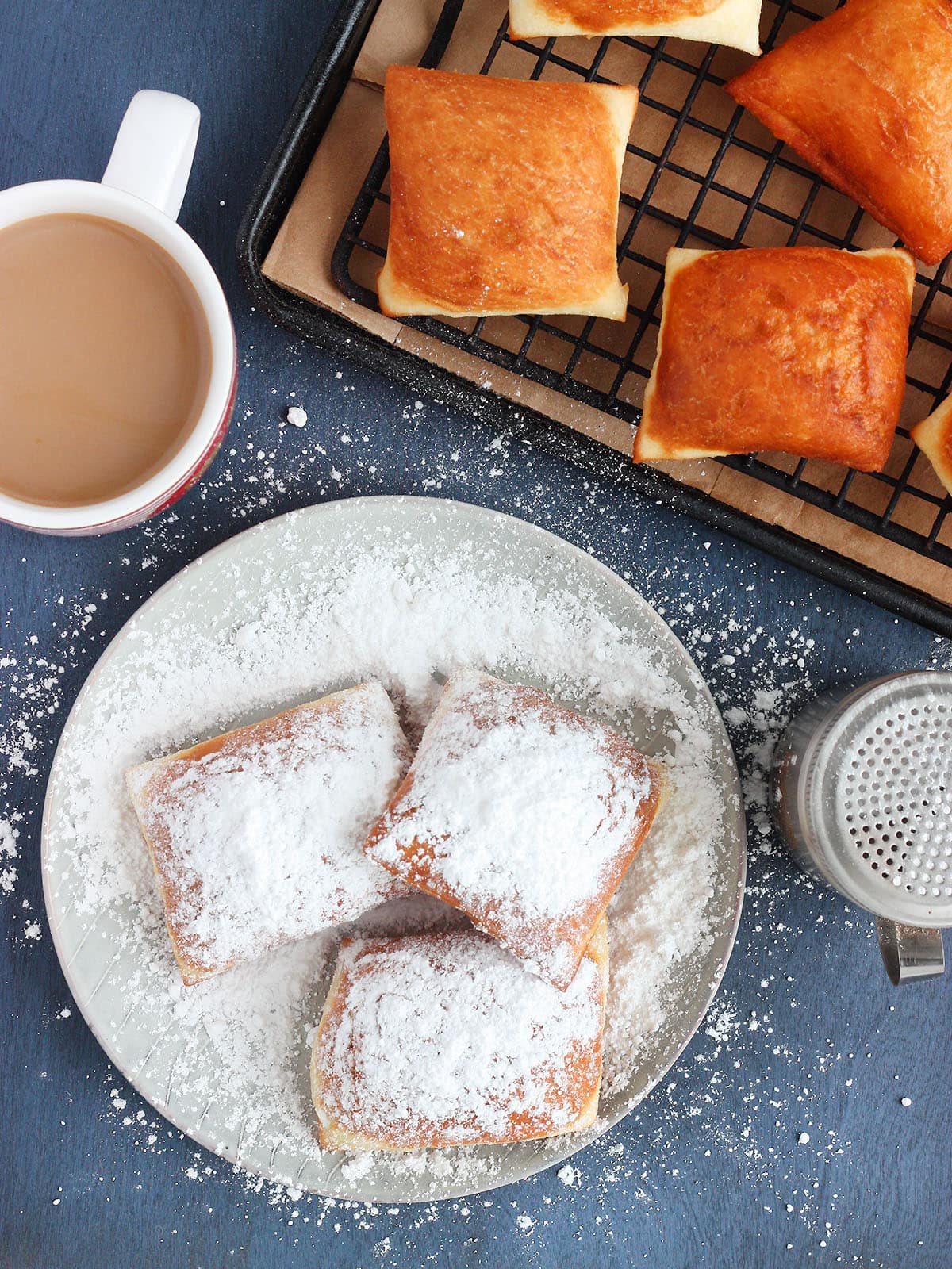 beignets on a grey plate covered in powdered sugar with a mug of cafe au lait on the side