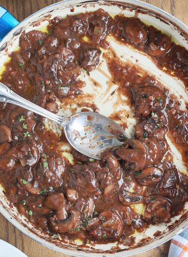 pan of red wine mushroom sauce for steak with a glass of red wine on the side.