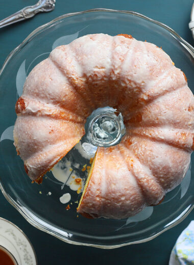 Apricot nectar cake on a clear glass cake pedestal with one slice removed.