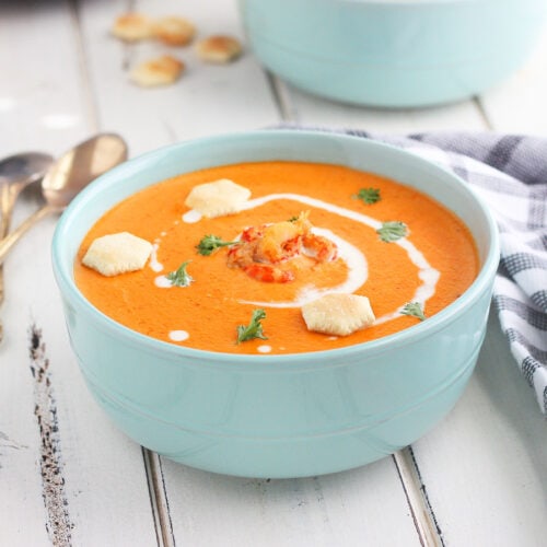 bowl of crawfish bisque garnished with cream, parsley and oyster crackers on a white wooden background