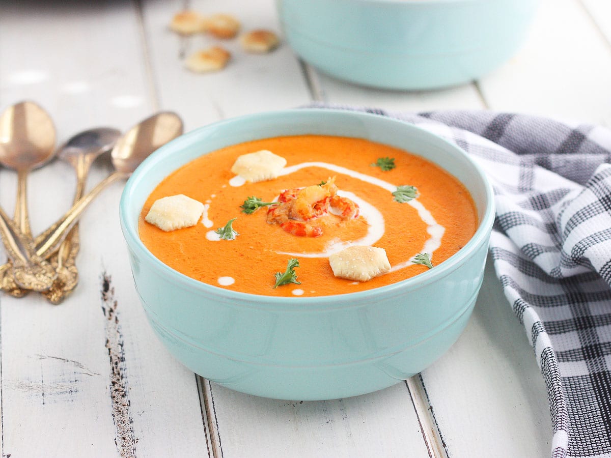 bowl of crawfish bisque garnished with cream, parsley and oyster crackers on a white wooden background