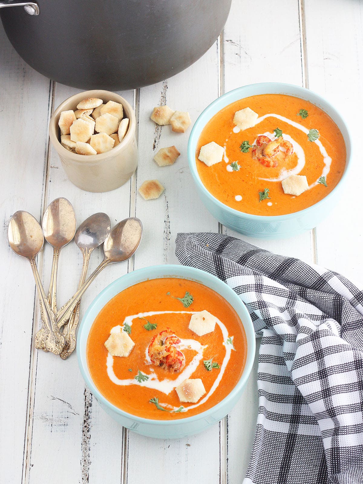 two bowls of crawfish bisque garnished with cream, parsley and oyster crackers on a white wooden background