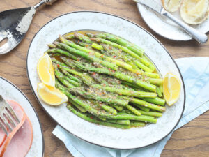 marinated asparagus in a white decorative serving dish with lemon wedges on the side